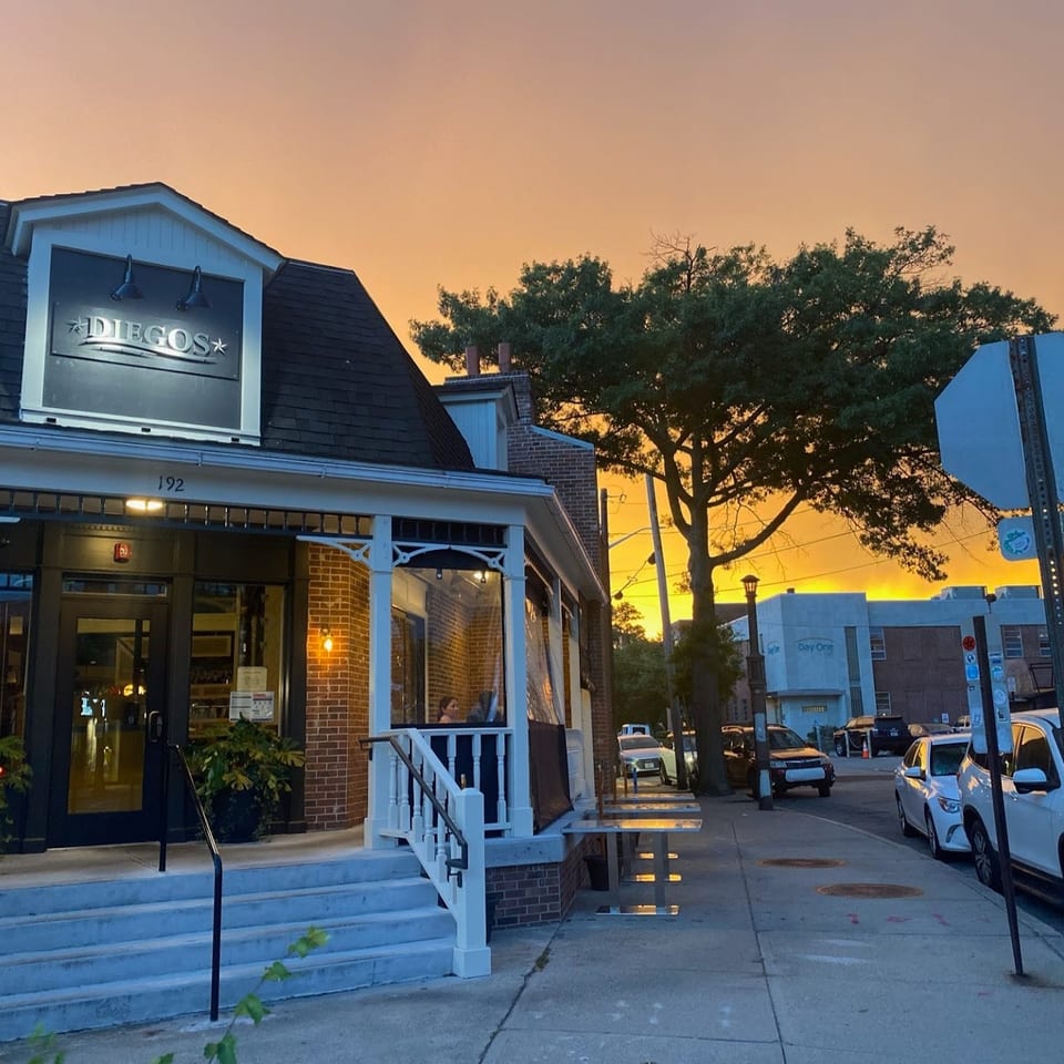 Diegos restaurant storefront at sunset, featuring brick walls, front steps, street parking, and a tree-lined urban sidewalk.