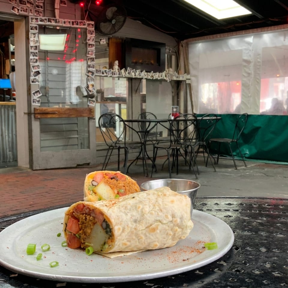 Stuffed burrito and cut-open half on a plate at an outdoor restaurant patio with string lights and café tables.