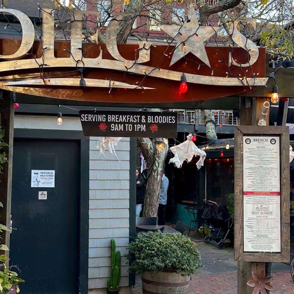 Rustic outdoor entrance to Tripp's restaurant, decorated with string lights, menus, patio seating, and a sign serving breakfast and bloodies.