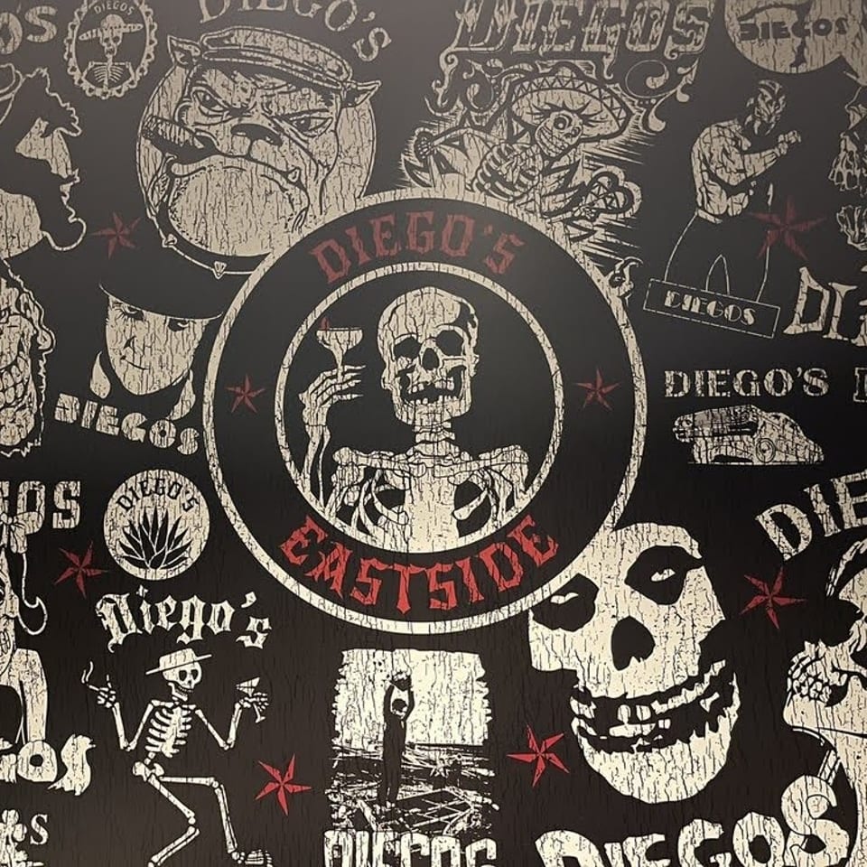 Black-and-cream Diego’s Grillhouse mural featuring skulls, skeletons, masked characters, and bold red lettering.