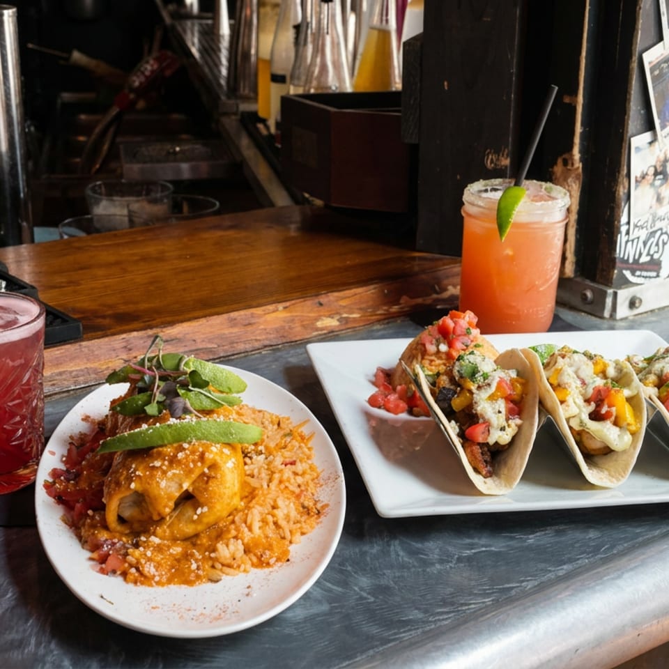 Tacos, saucy rice, and colorful cocktails arranged on a bar beside Tabasco bottles and a photo display.