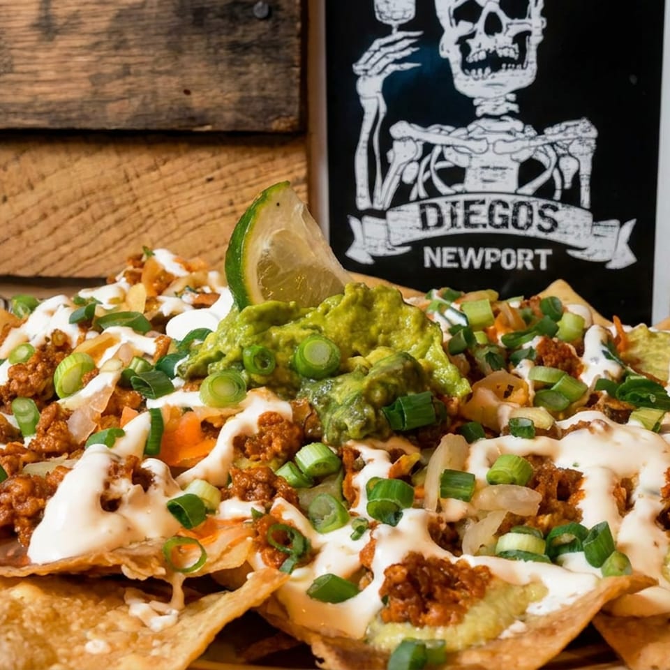 Loaded nachos topped with ground meat, guacamole, cheese sauce, green onions, and lime, served before a Diegos Newport sign.